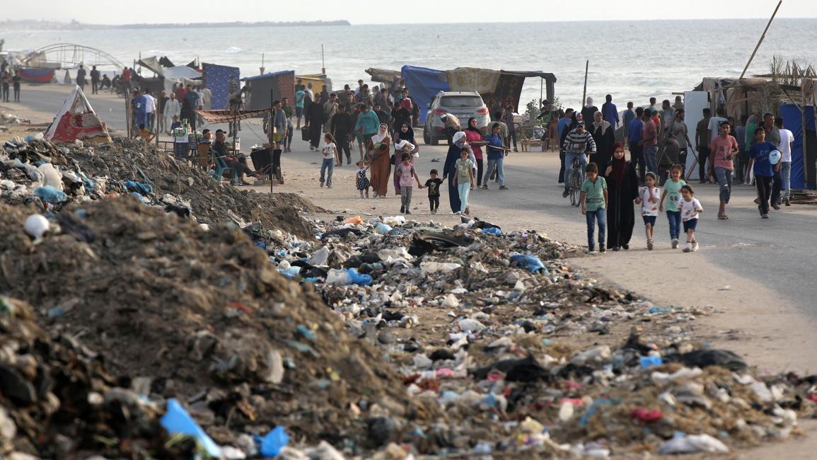 النازحون يسيرون بجوار أكوام القمامة (أشرف عمرة / Getty)